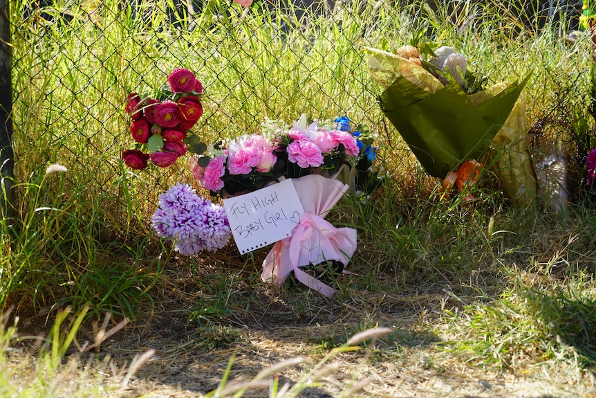 Flowers on a fence with a note reading fly high baby girl