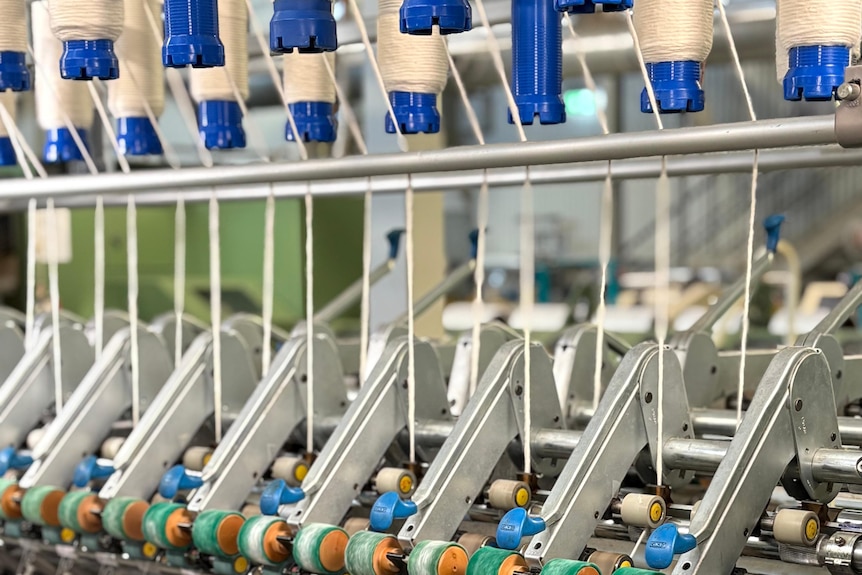 Thicker yarn in spools are being processed into thinner yarn on spools