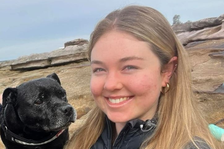 A smiling young blonde woman with a black dog.