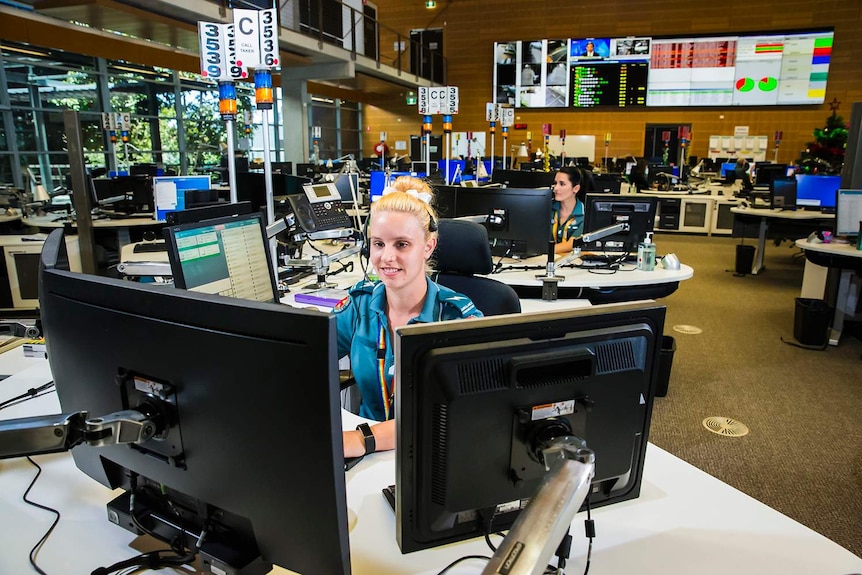 Two emergency medical dispatchers sitting at a desk with computer screens in the Brisbane Operations Centre.