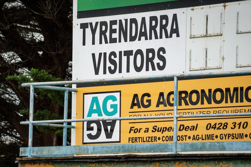 A football score billboard with "TYRENDARRA" and "VISITORS".