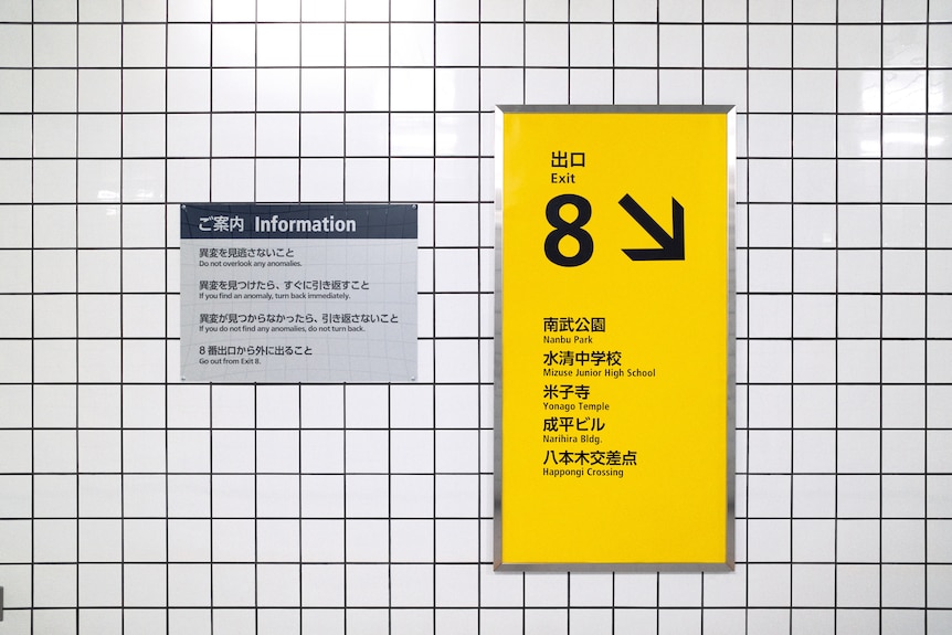 A tiled wall with two signs, a yellow directional sign and a smaller white sign with information.