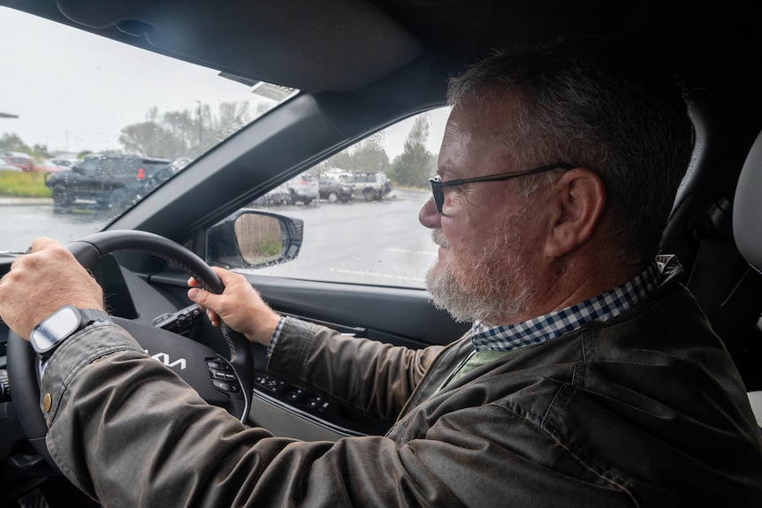 A man sitting in a car, with his hands on the steering wheel