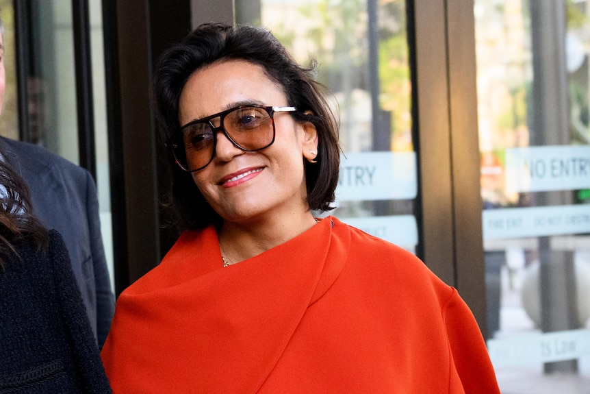 Amanda Ghost smiles outside court, while wearing a red top and sunglasses.