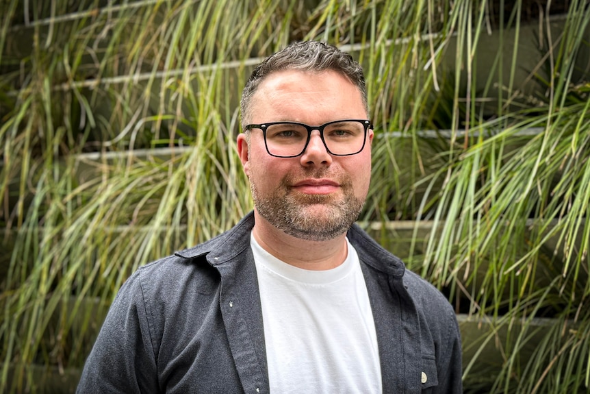 A man standing in front of a green background. 