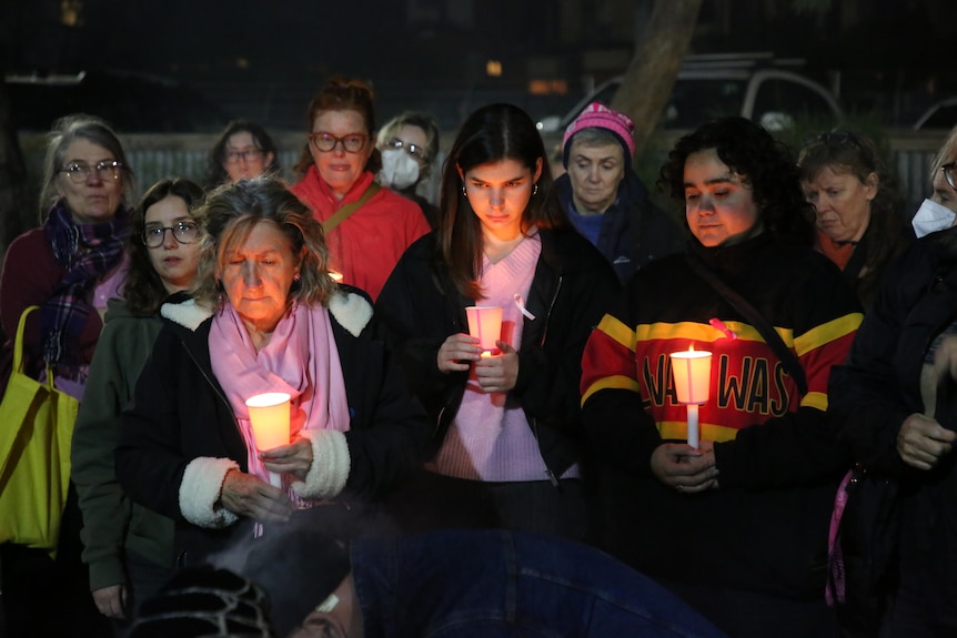 A crowd of about a dozen holding candles, looking solemn, at a vigil.