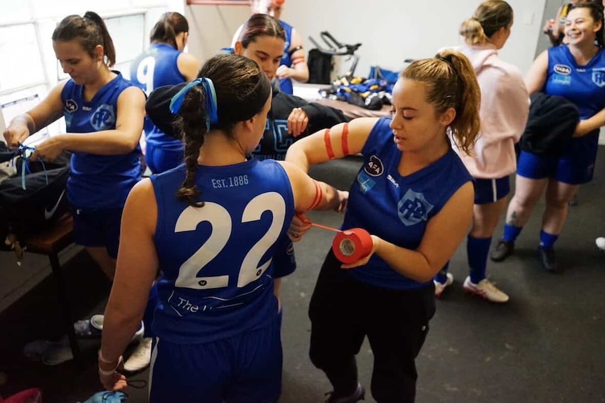 Women's footy players putting red armbands on each other in club rooms.