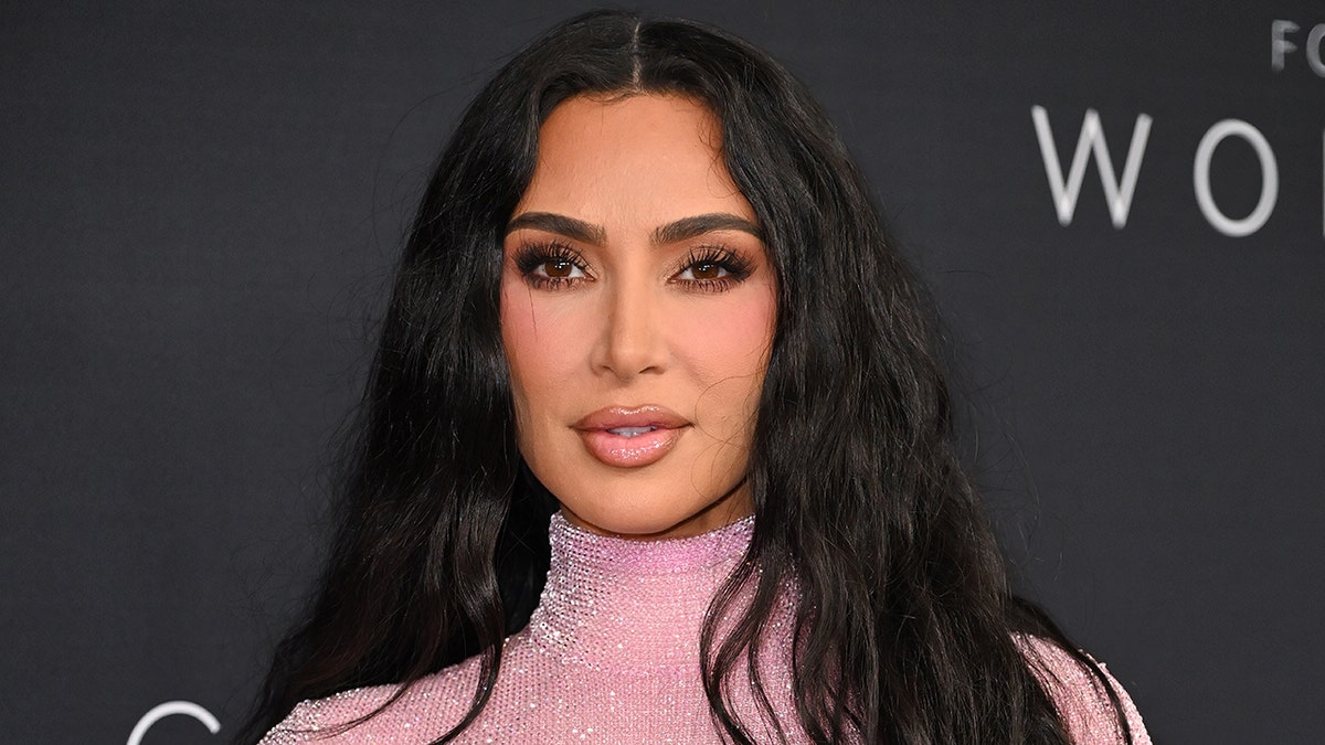 Kim Kardashian smiling and walking on a red carpet wearing a pink dress