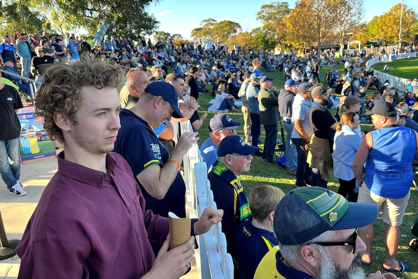 Young man smiles among a crowd of football spectators on a grassy hill