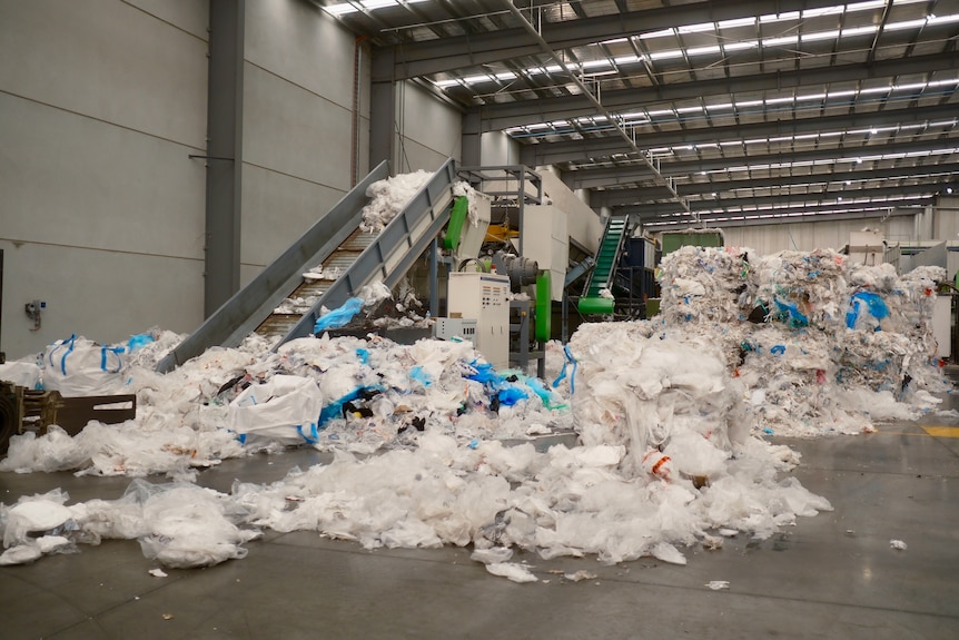 Piles of clear soft plastics lay scattered over the floor of a shed and pile beside a conveyor belt.