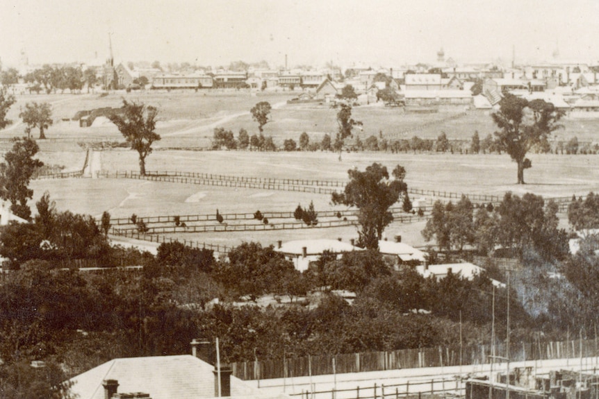 A black and white image of buildings with large empty grass area between.