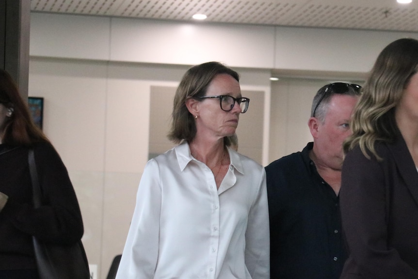 A woman with short hair and wearing a white top leaves the court after a trial.