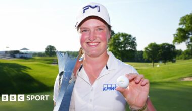 Lottie Woad smiling and holding a trophy and a golf ball
