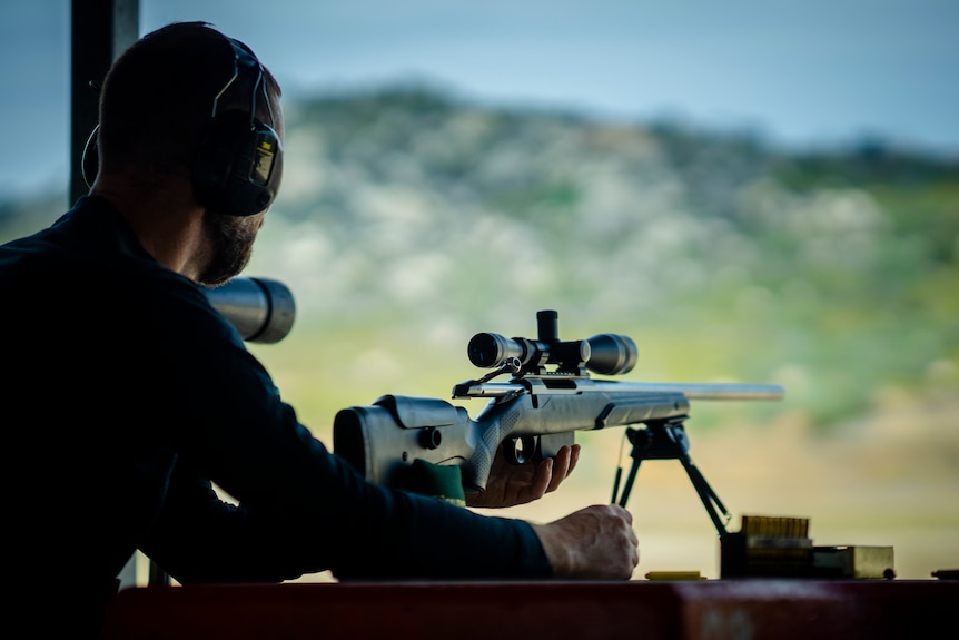 A man sits behind a rifle at a shooting range.