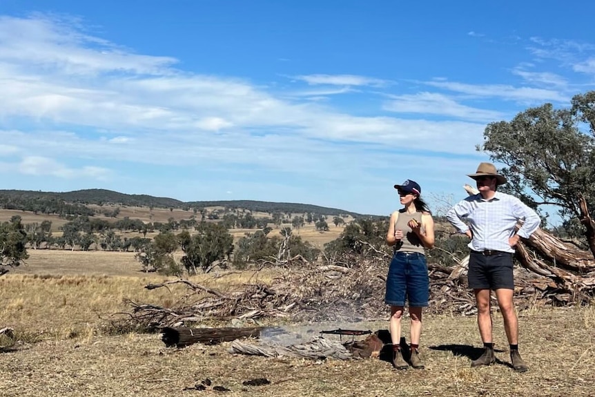 Two people standing on the land, looking to the left.