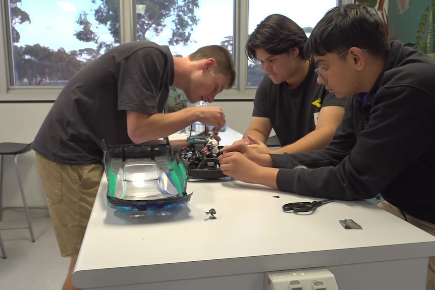 Three teens standing around an RC car with its shell off while they screw in components