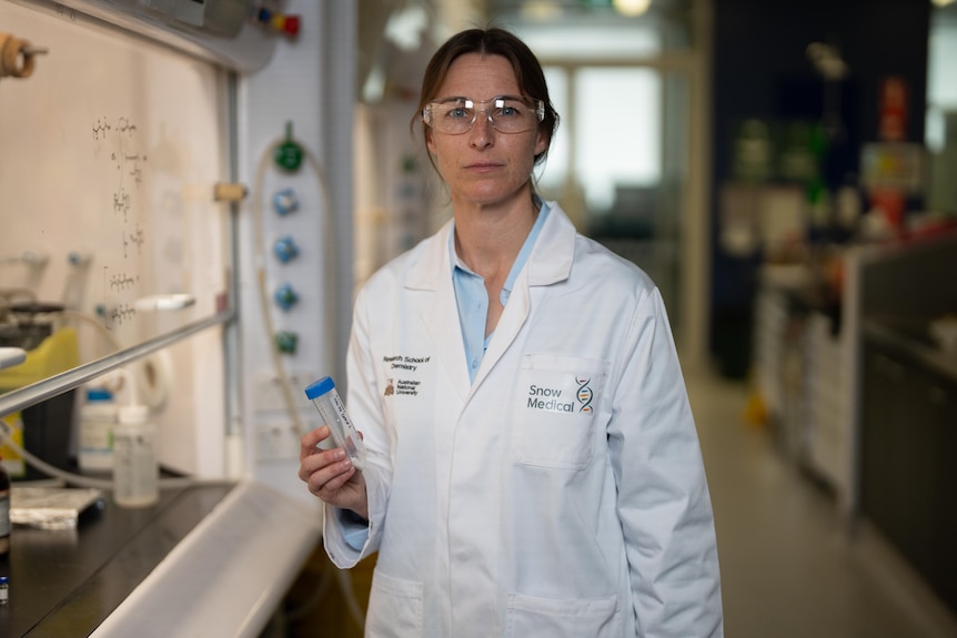 A woman in a lab coat holding a clear tube in a laboratory.