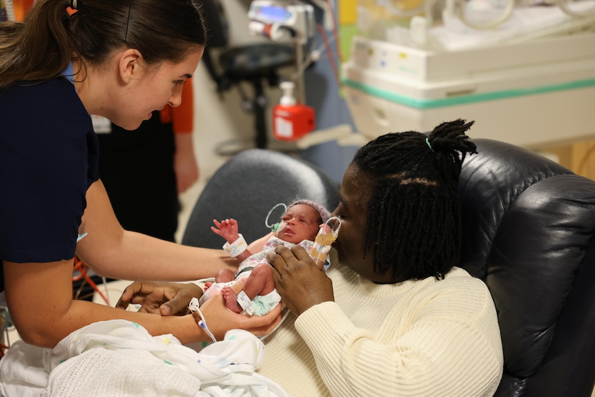 A nurse hands a newborn baby to a woman