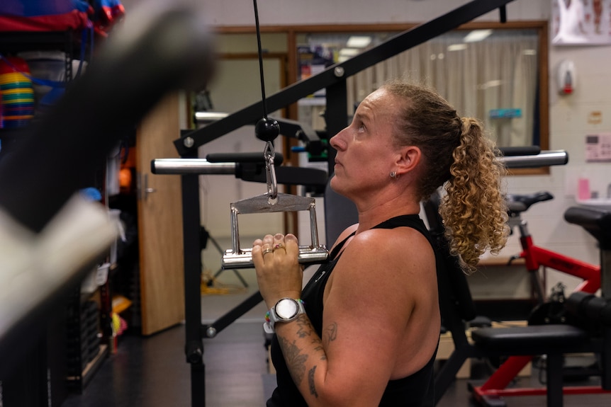 A profile shot of a woman with curly hair pulling down on some weights.