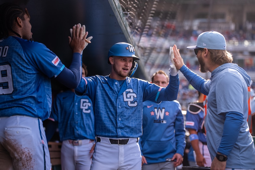 Curtis Mead, in blue kit, high-fives his teammates in the dugout at a baseball game.