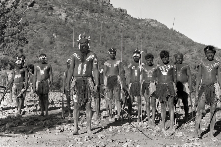 A black and white photo of Aboriginal actors dressed in approximately historical clothing in the outback.