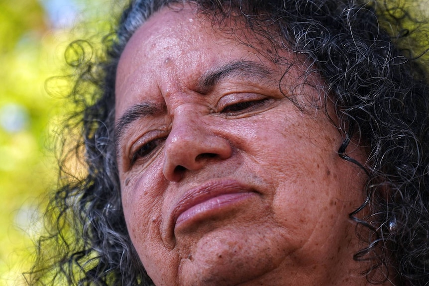 Close up of a woman with dark-brown curly hair looking down.