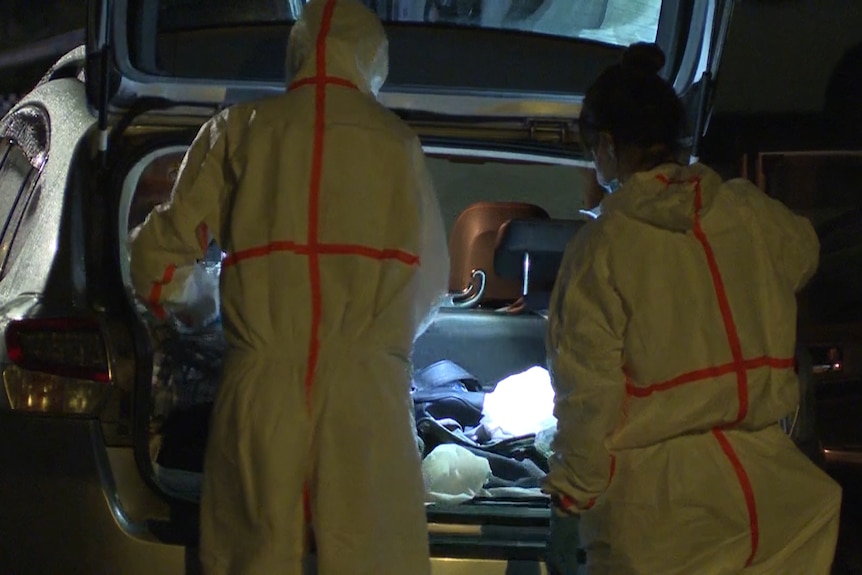Two investigators in protective suits search the contents inside the boot of a hatchback.