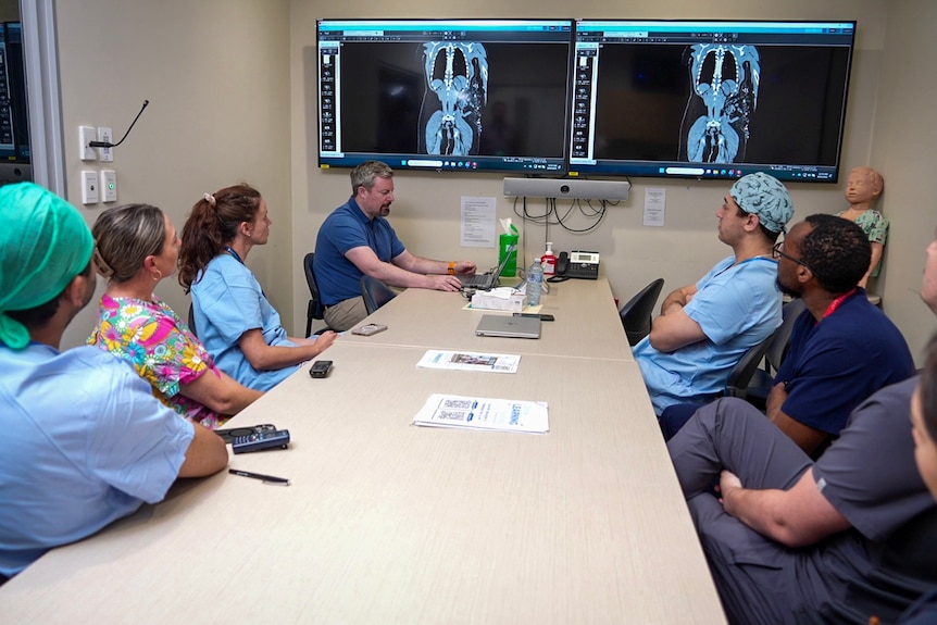 A group of people in hospital scrubs examine CT scans.