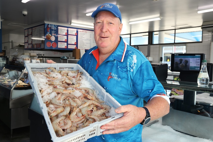 Fish monger holds up tray of banana prawns.