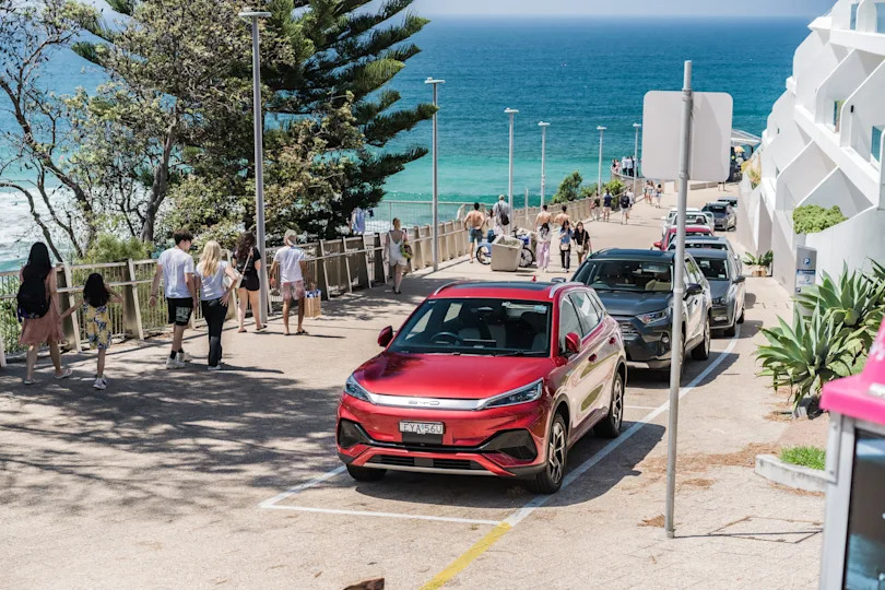 A bustling street scene by the ocean with people walking on the sidewalk.