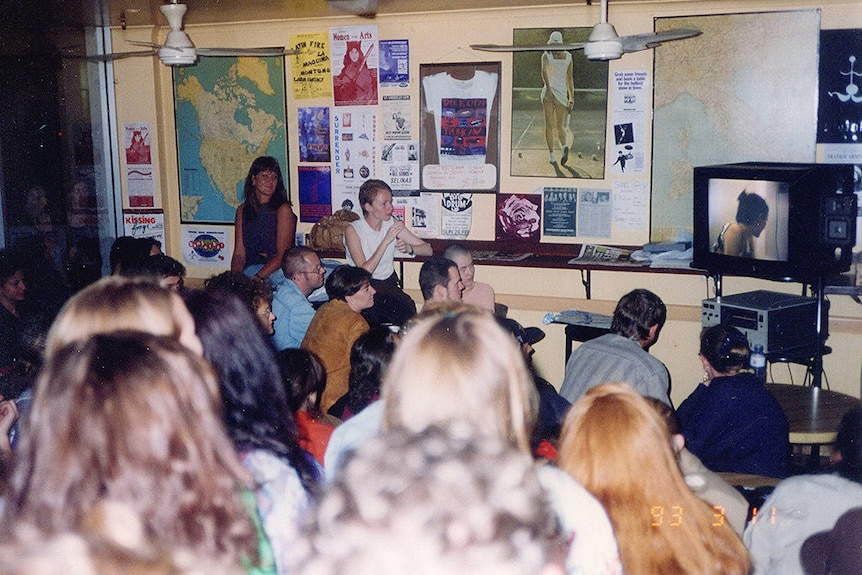 A crowd of people watch a television.