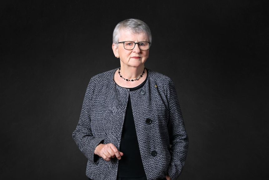 Virginia Bell has short grey hair and glasses, and gestures with her right hand.