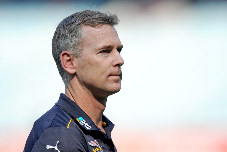 A man in a navy blue polo shirt looks serious.