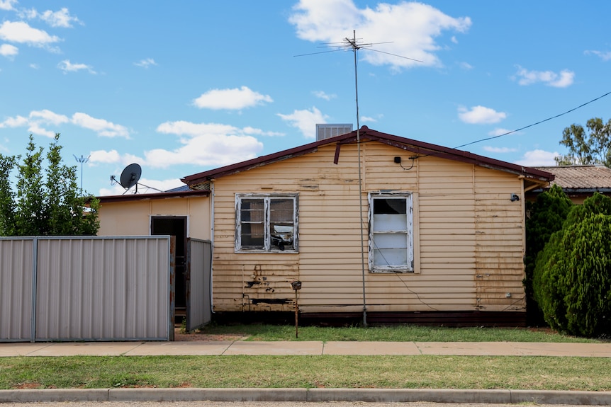 Aside on view of a cream coloured weatherboard house, some plans of wood are rotting and window panes are broken.