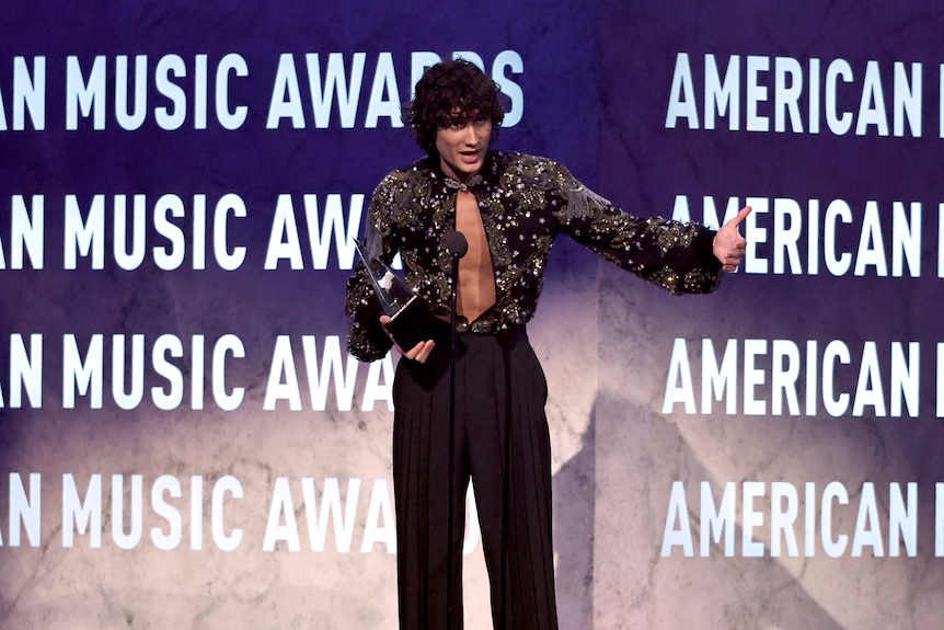 A man in a sparkly top speaks into a mic.