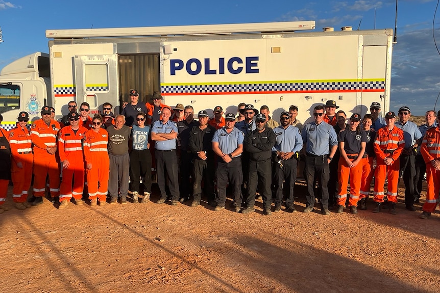 A group of emergency services standing behind a police vehicle.