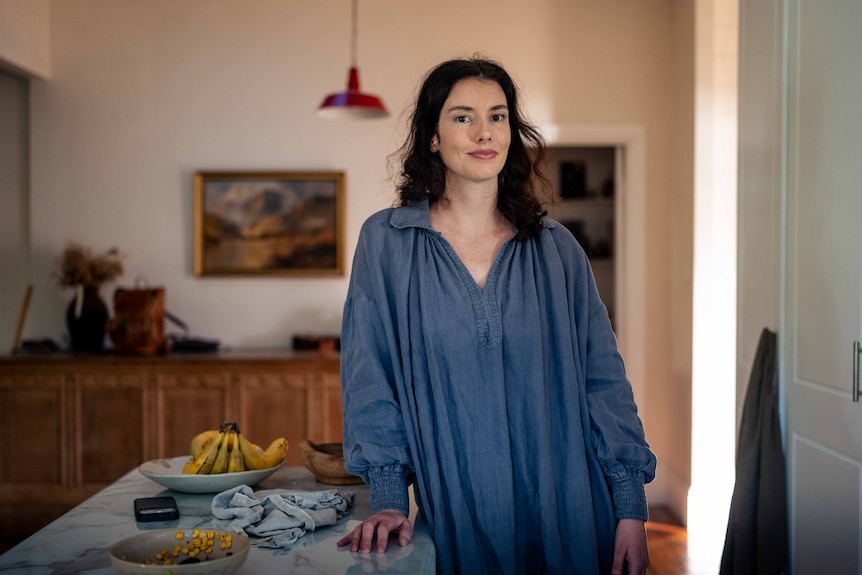 A woman leans against the kitchen bench, posing for a photo