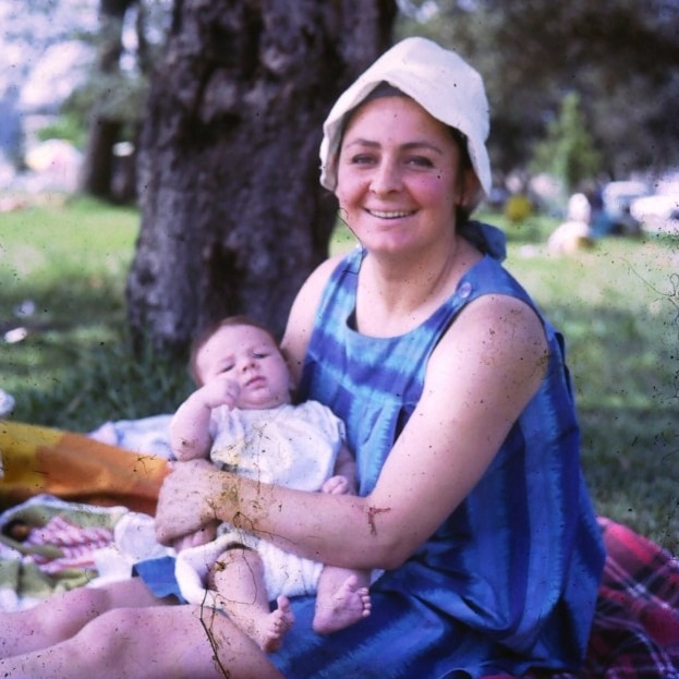 A woman wearing a blue outfit sits holding a baby.