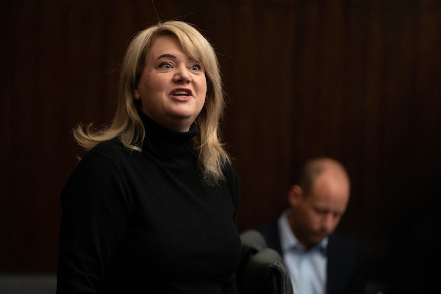 A blonde politician in parliament smiling at the camera.