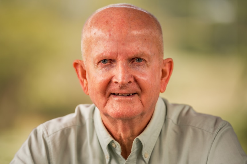 Older man in a light green business shirt sitting in a park.