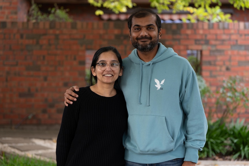 A woman and a man standing outside a house with a brick fence