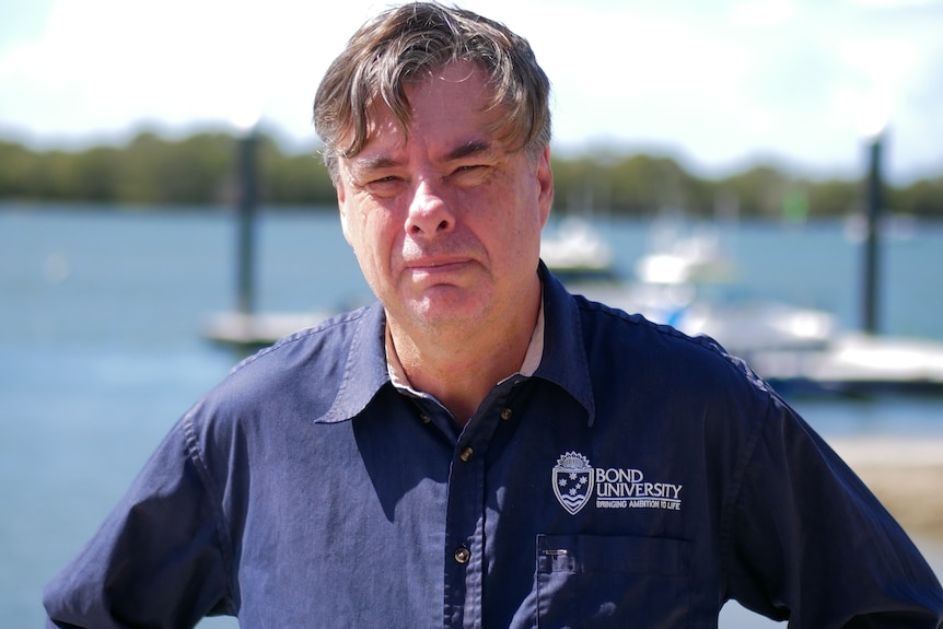 A man in a bond university branded shirt stands at a marina