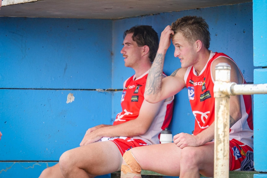 A man scratches his head while sitting on a football bench