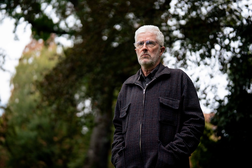 Man poses for photo with greenery behind him
