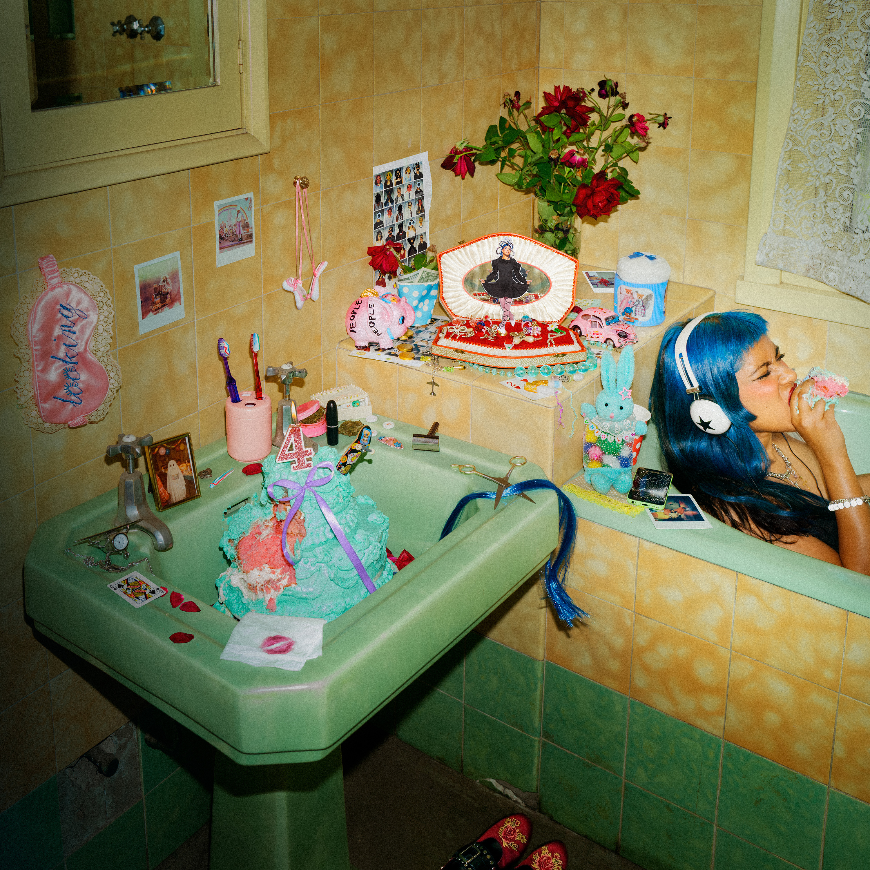 Vintage bathroom littered with trinkets & decoration. Sri-Lankan Australian woman, blue hair lies in bath with headphones on.