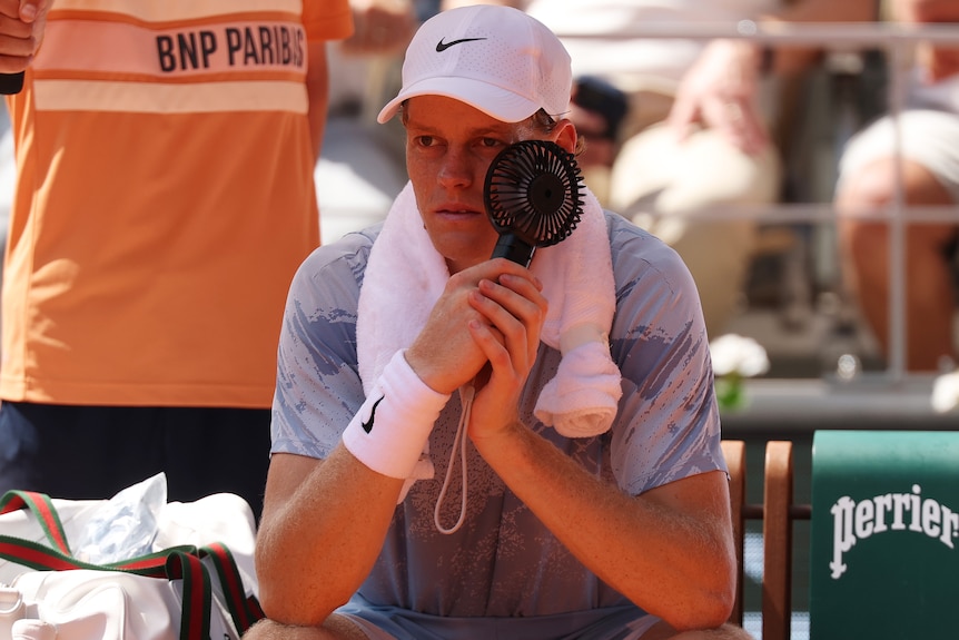 Jannik Sinner uses a handheld fan in attempt to cool down during a break in play at the French Open.