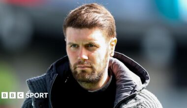 Brighton boss Fabian Hurzeler, in a hooded jacket and with dark brown hair and beard, looks on before a Premier League match at Burnley