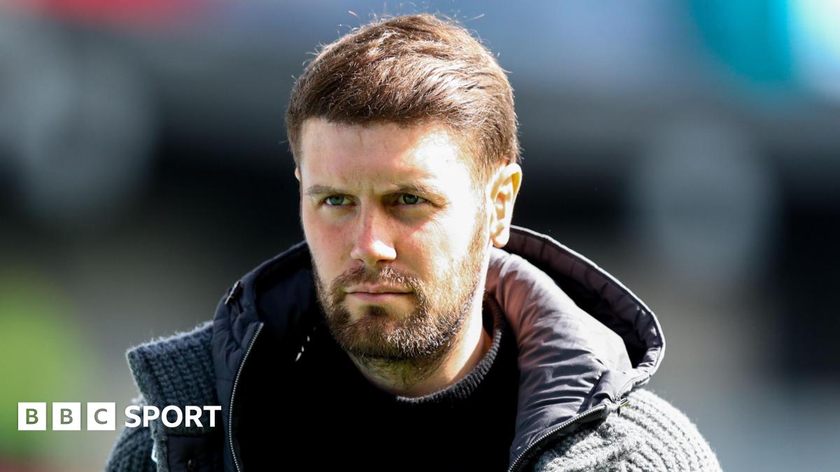 Brighton boss Fabian Hurzeler, in a hooded jacket and with dark brown hair and beard, looks on before a Premier League match at Burnley
