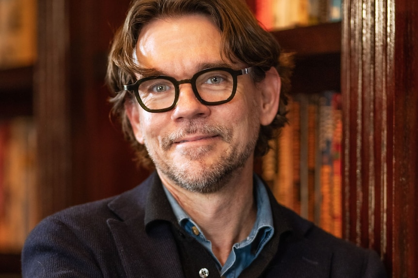 a man in black glasses and a navy jacket with dark hair