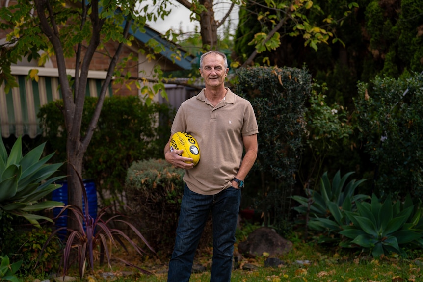 An Adelaide resident holding a football at his suburban home.